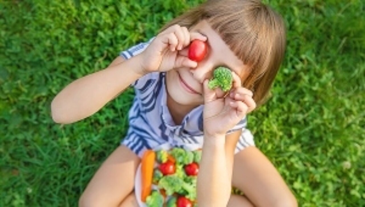 Ein Kind hält sich eine Tomate und ein Stück Brokkoli vor die Augen.