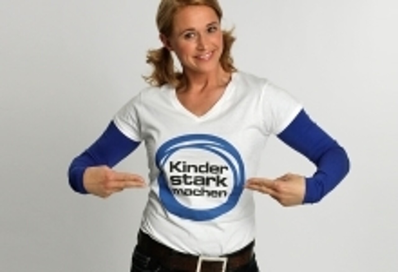 Singa zeigt auf das „Kinder stark machen“-Logo auf ihrem T-Shirt