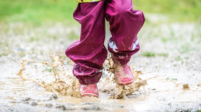 Ein Kind mit Gummistiefeln springt in eine Pfütze
