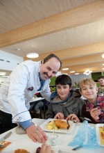 food@ucation Johann Lafer und zwei Jungs mit Mittagessen auf dem Tisch in der Schulmensa