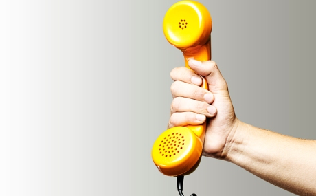 Hand hält gelben Telefonhörer vor grauem Hintergrund