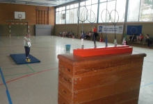 Kind steht auf der Matte und wirft mit Bällen auf feststehende Badminton-Schläger.
