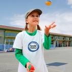 Mädchen in im „Kinder stark machen“-T-Shirt jongliert mit Bällen vor der Schule