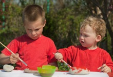 Jungs bemalen Steine Zwei Jungs mit roten T-Shirts bemalen mit einem Pinsel Steine