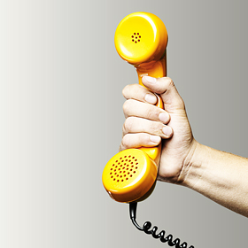 Hand hält gelben Telefonhörer vor grauem Hintergrund