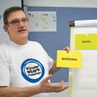Kursleiter im „Kinder stark machen“-T-Shirt spricht vor einer Flipchart