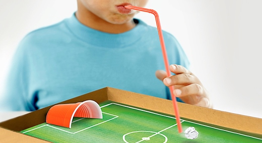 Kind pustet mit Strohhalm Papierball auf Fußballfeld