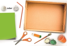 Bastelmaterial grünes Papier, Schere, Kleber, Farbe, Pinsel, Bälle, Becher, Schachtel
