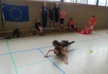 Zwei Kinder liegen übereinander auf einem Rollbrett und durchfahren einen Parcours.