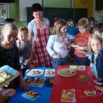 Lehrerin in Kochschürze bereitet mit einer Gruppe von Schülern ein Essen zu