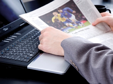 aufgeschlagene Zeitung mit einem Sportbild liegt auf geöffnetem Laptop