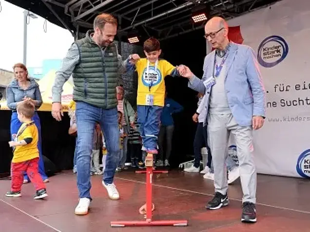 Robert Voigtsberger und Dr. Johannes Nießen reichen einem Jungen beim Balancieren eine helfende Hand.