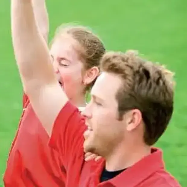 Ein Trainer und ein dahinter stehendes Mädchen hebn den rechten Arm