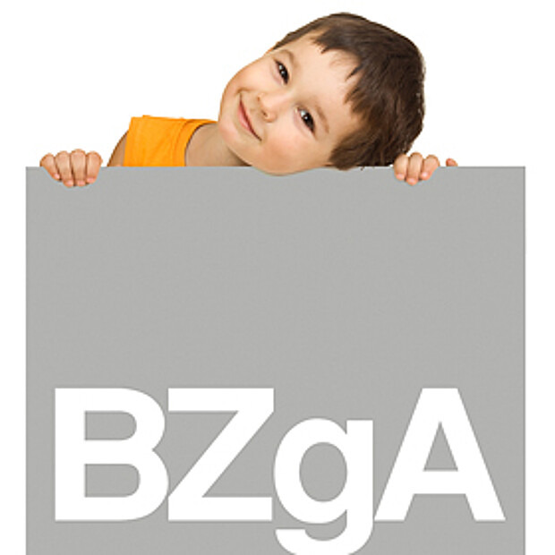 Junge lächelt und hält ein Schild mit BZgA Logo