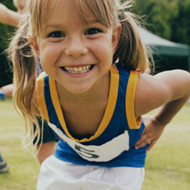 Mädchen im Kindergartenalter in Leichtathletik-Kleidung lächelt in die Kamera
