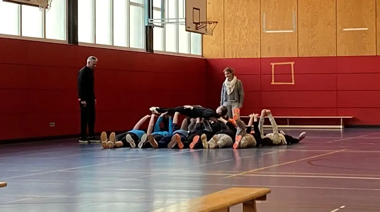 Die Teilnehmerinnen und Teilnehmer tragen im Liegen eine Person auf ihren Armen.