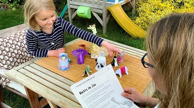 Mädchen spielt mit Zoo-Tieren und eine Frau hält ein Blatt in der Hand