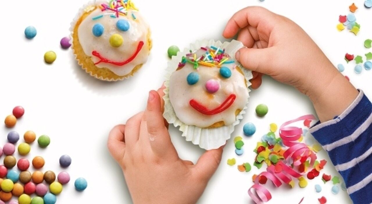 Kinderhand hält Muffin als bunten Clown verziert