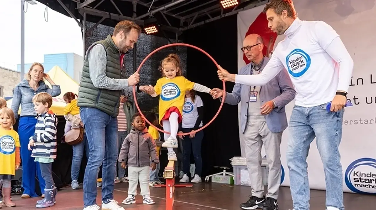 Dr. Nießen und Dezernent Voigtsberger geben einem Kind beim Balancieren Hilfestellung.