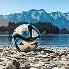Kinderfußball auf großen Kieseln vor See- und Bergpanorama