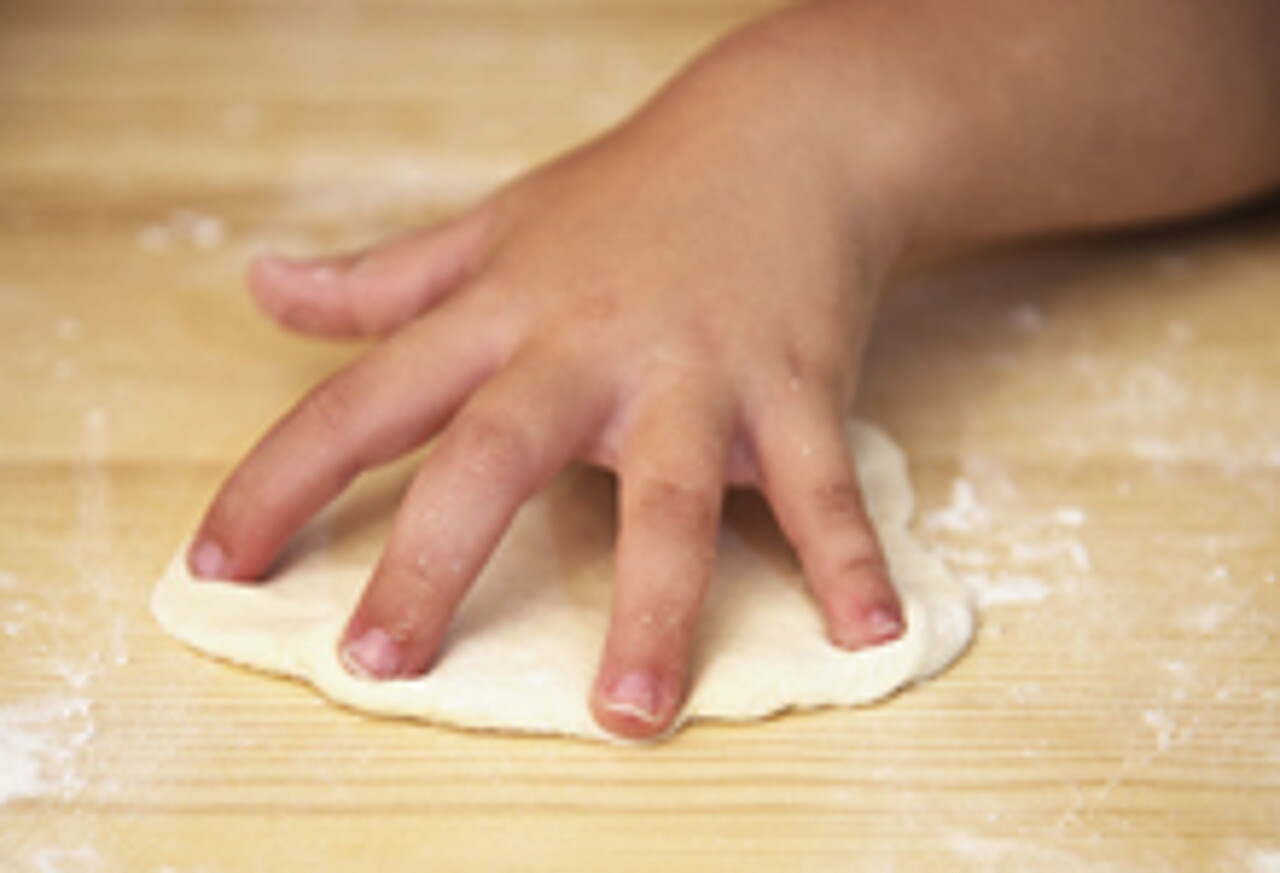 Kinderhand rollt Pizzateig aus