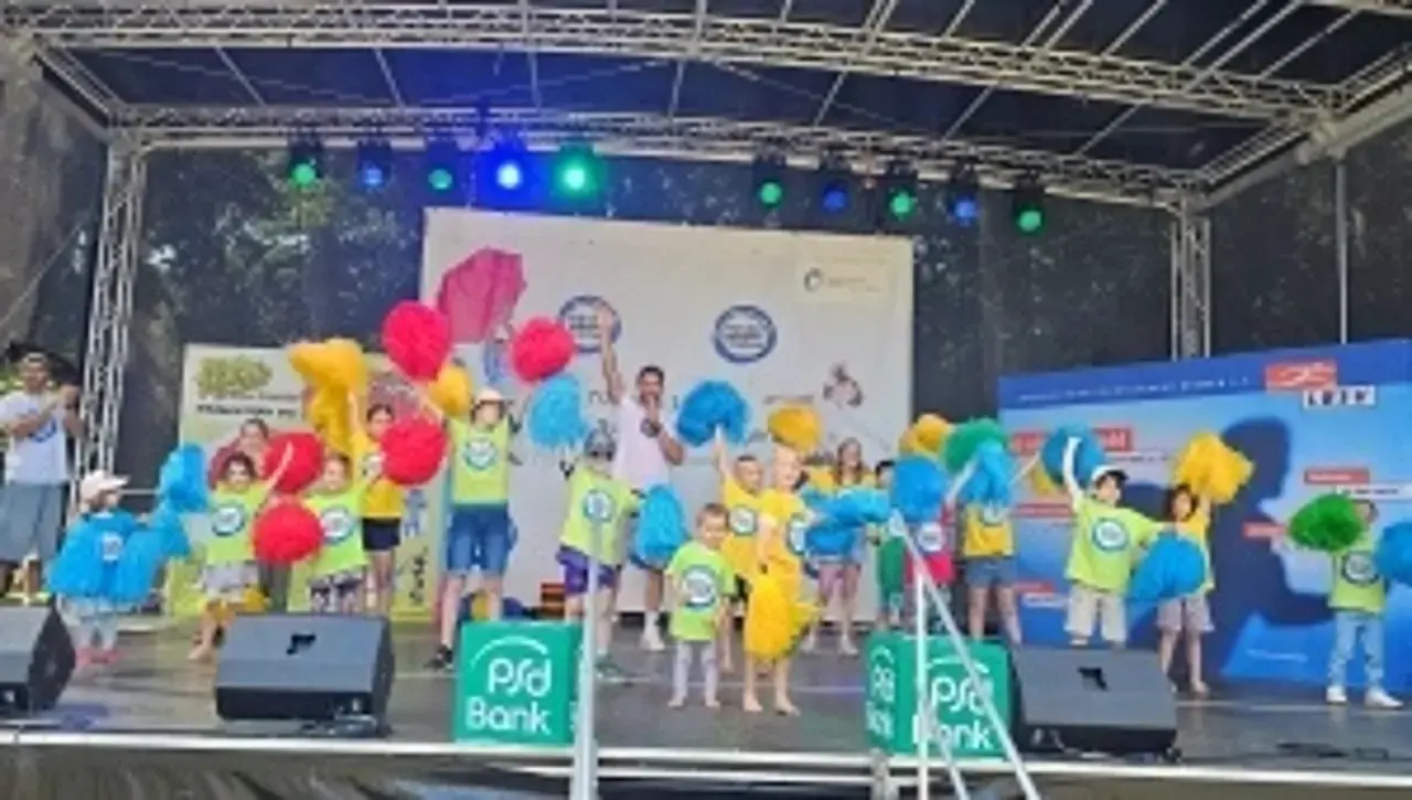 Kinder tanzen auf einer Bühne mit bunten Cheerleader-Puscheln.