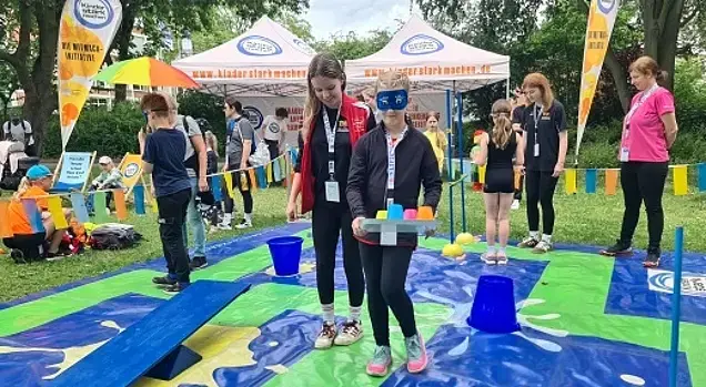 Im Vertrauensparcours führt ein Kind ein zweites, das die Augen verbunden hat.