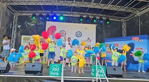Kinder tanzen auf einer Bühne mit bunten Cheerleader-Puscheln.