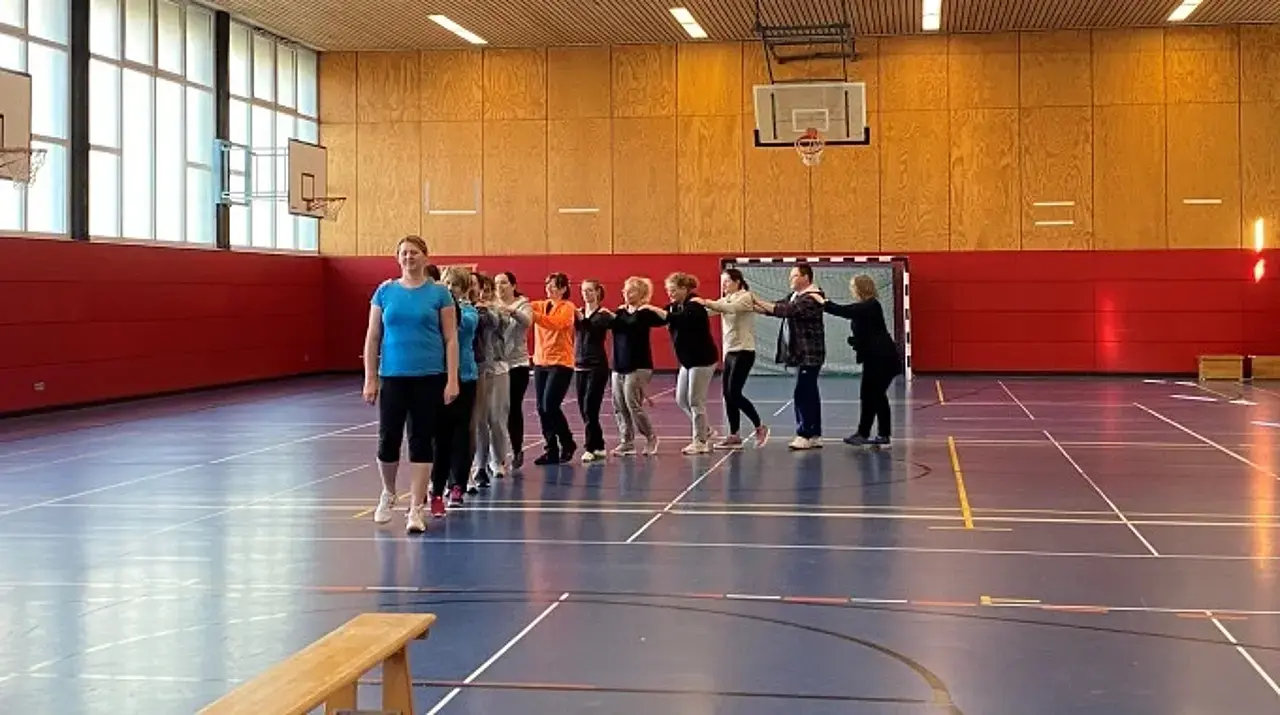 Die Teilhehmerinnen und -teilnehmer haben sich an den Schultern gefasst und vollführen eine Polonaise durch die Halle.