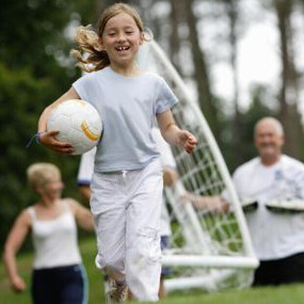 Mädchen läuft mit Fußball unterm Arm auf einem Fußballfeld