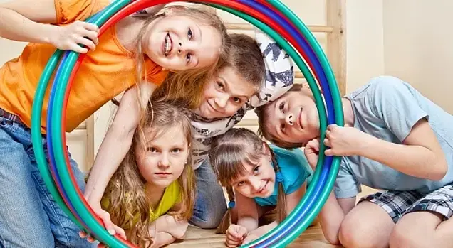 Fünf fröhliche Kinder stecken ihre Köpfe durch farbenfrohe Hula-Hoop-Reifen.