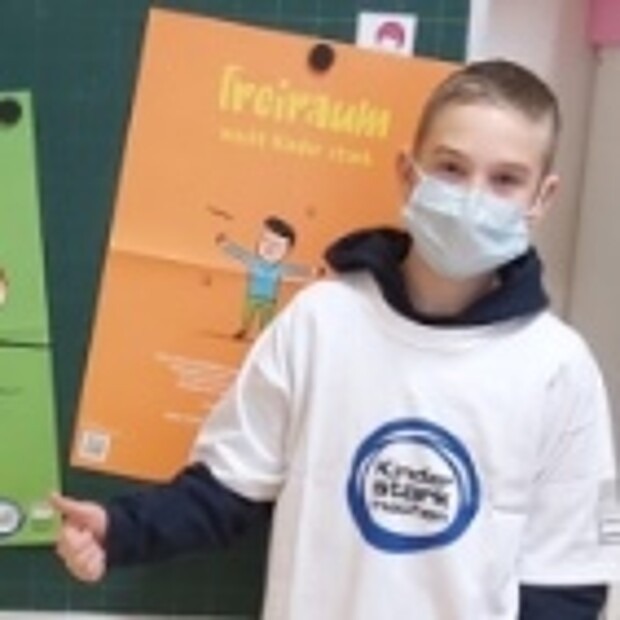 Ein Junge mit Kinder stark machen Shirt steht vor einem Plakat