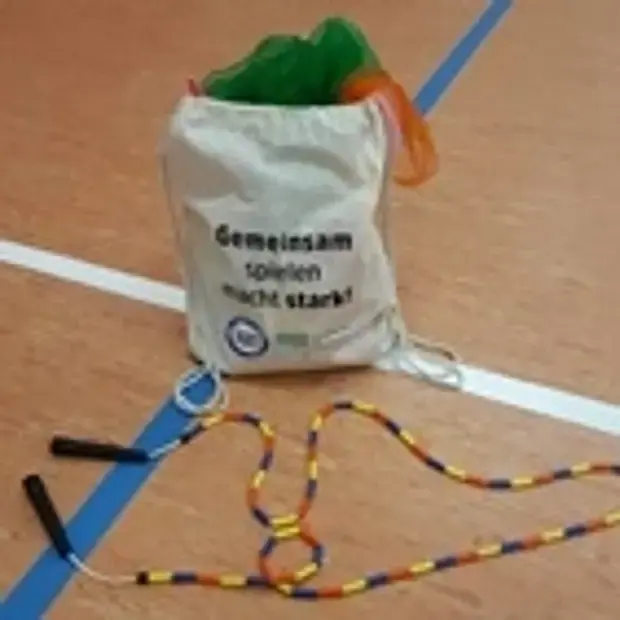 Auf dem Boden einer Sporthalle liegen ein Kinder stark machen Sportbeutel und ein Springseil