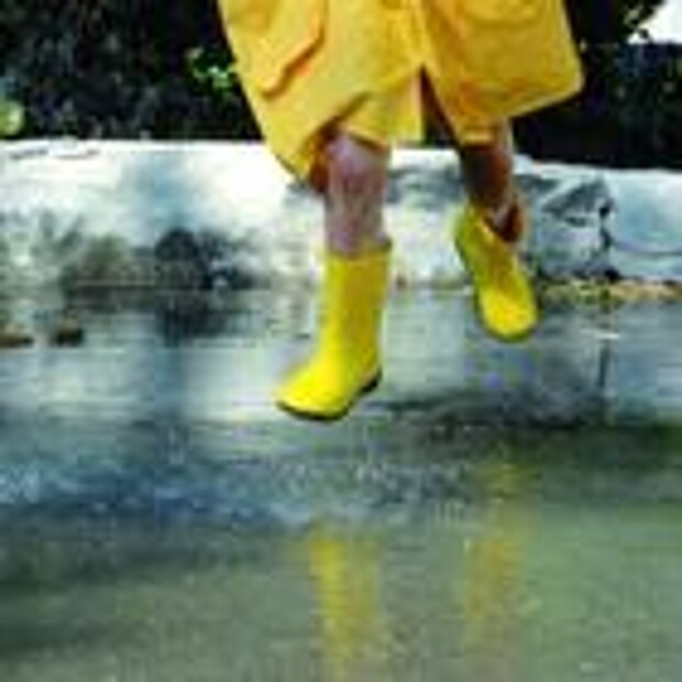 Kind in gelbem Regenmantel und mit gelben Gummistiefeln springt in eine Pfütze