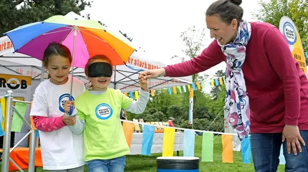 Ein Kind wird von einem weiterem Kind und der Mutter mit verbundenen Augen durch den Vertrauensparcours geführt.