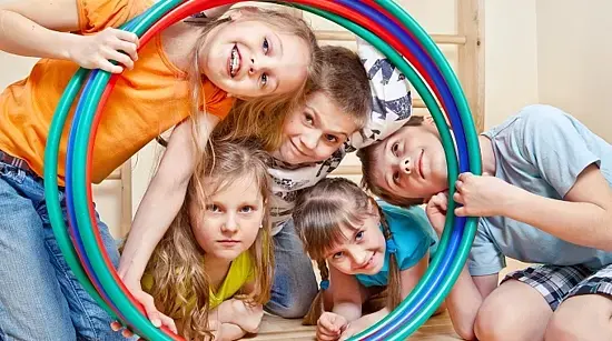Fünf fröhliche Kinder stecken ihre Köpfe durch farbenfrohe Hula-Hoop-Reifen.