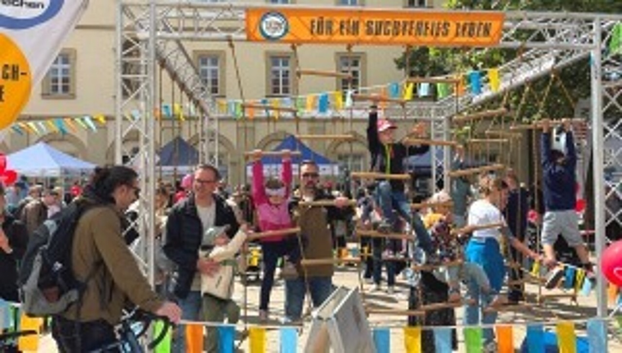 Kleine Kinder klettern im Klettergarten, Eltern geben Hilfestellung.