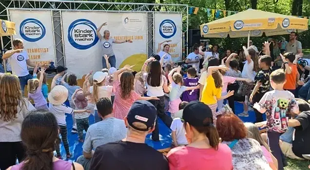 Kinder stark machen-Botschafterin Singa tanzt auf der Bühne. Die Kinder davor mit ihr.