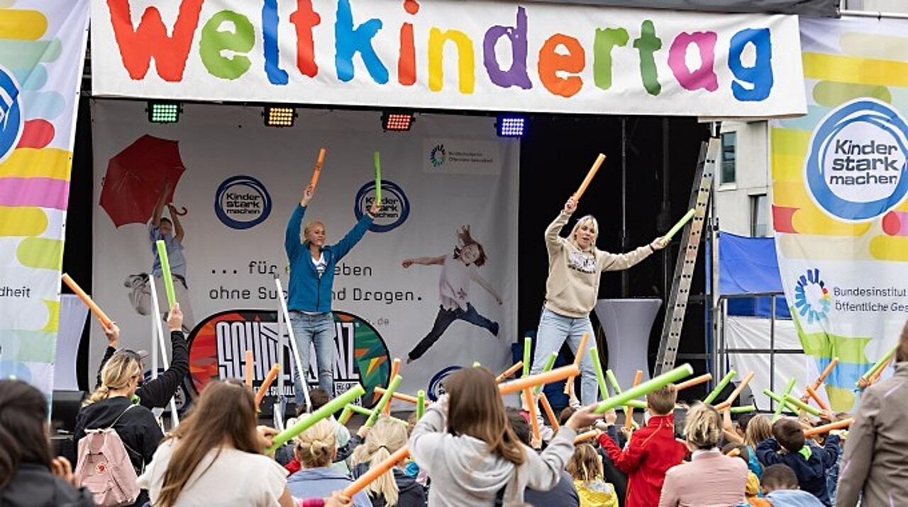 Singa und das Publikum schwingen bunte Stäbe über ihren Köpfen hin und her.