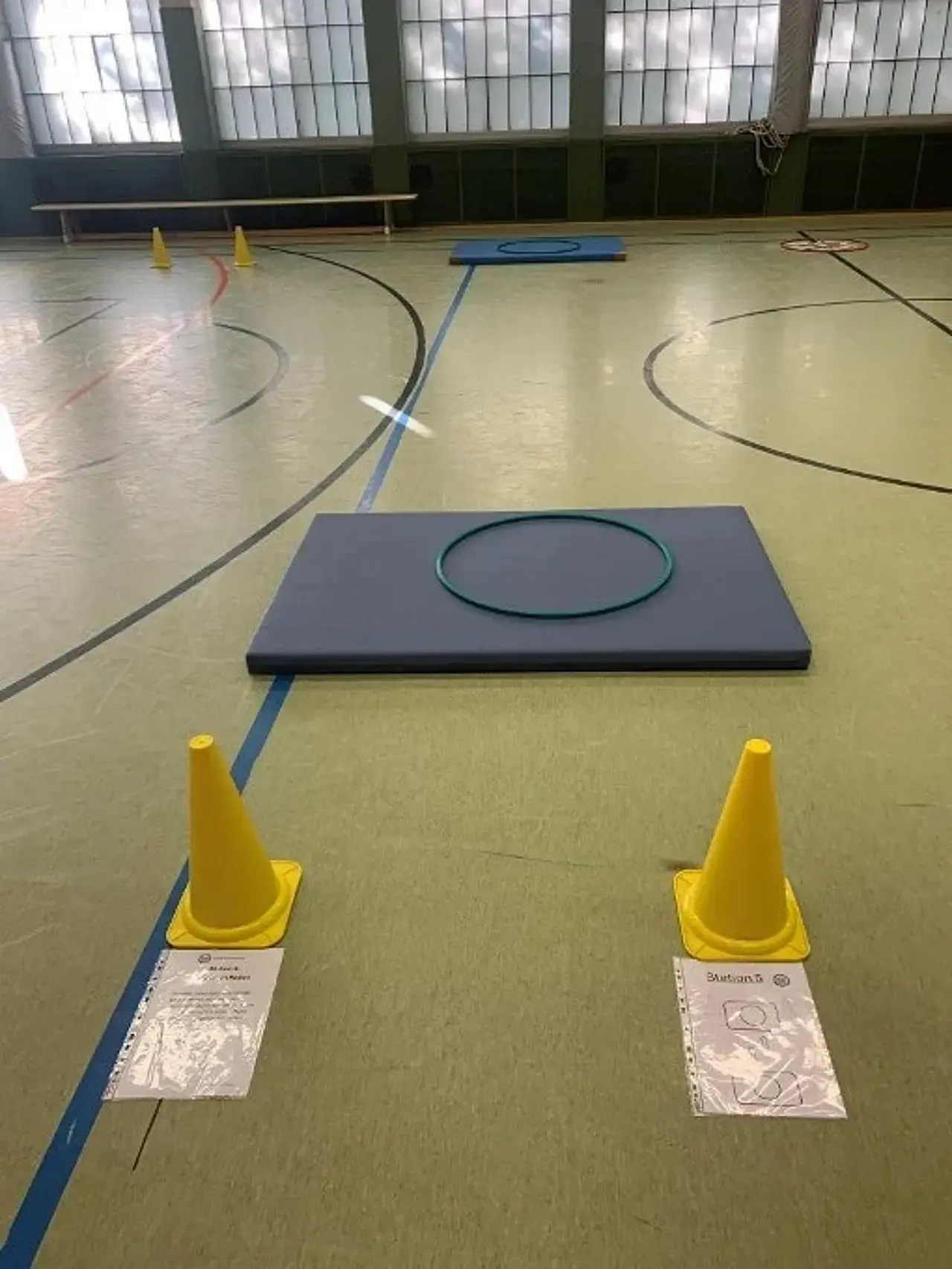 2 Turnmatten im 10m-Abstand auf dem Boden, auf beiden liegt ein Hula-Hoop-Reifen