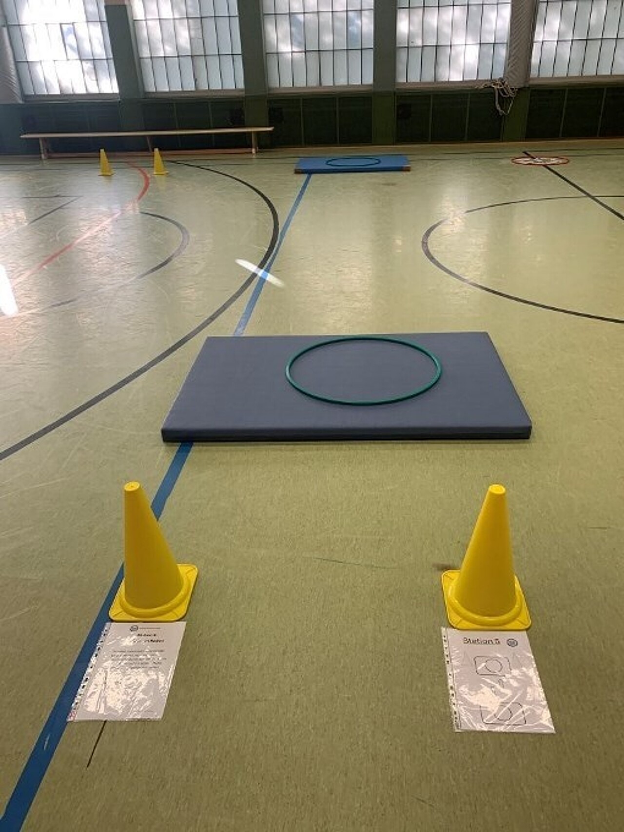 2 Turnmatten im 10m-Abstand auf dem Boden, auf beiden liegt ein Hula-Hoop-Reifen