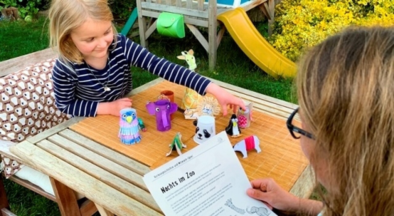 Mädchen spielt mit Zoo-Tieren und eine Frau hält ein Blatt in der Hand