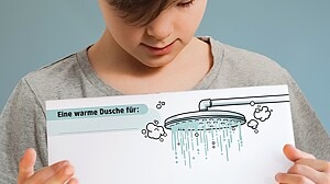 Ein Junge zeigt die PDF-Vorlage für die Warme Dusche mit einem Bild von einem Duschkopf, darunter viel Platz für positive Botschaften.