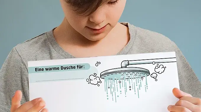 Ein Junge zeigt die PDF-Vorlage für die Warme Dusche mit einem Bild von einem Duschkopf, darunter viel Platz für positive Botschaften.