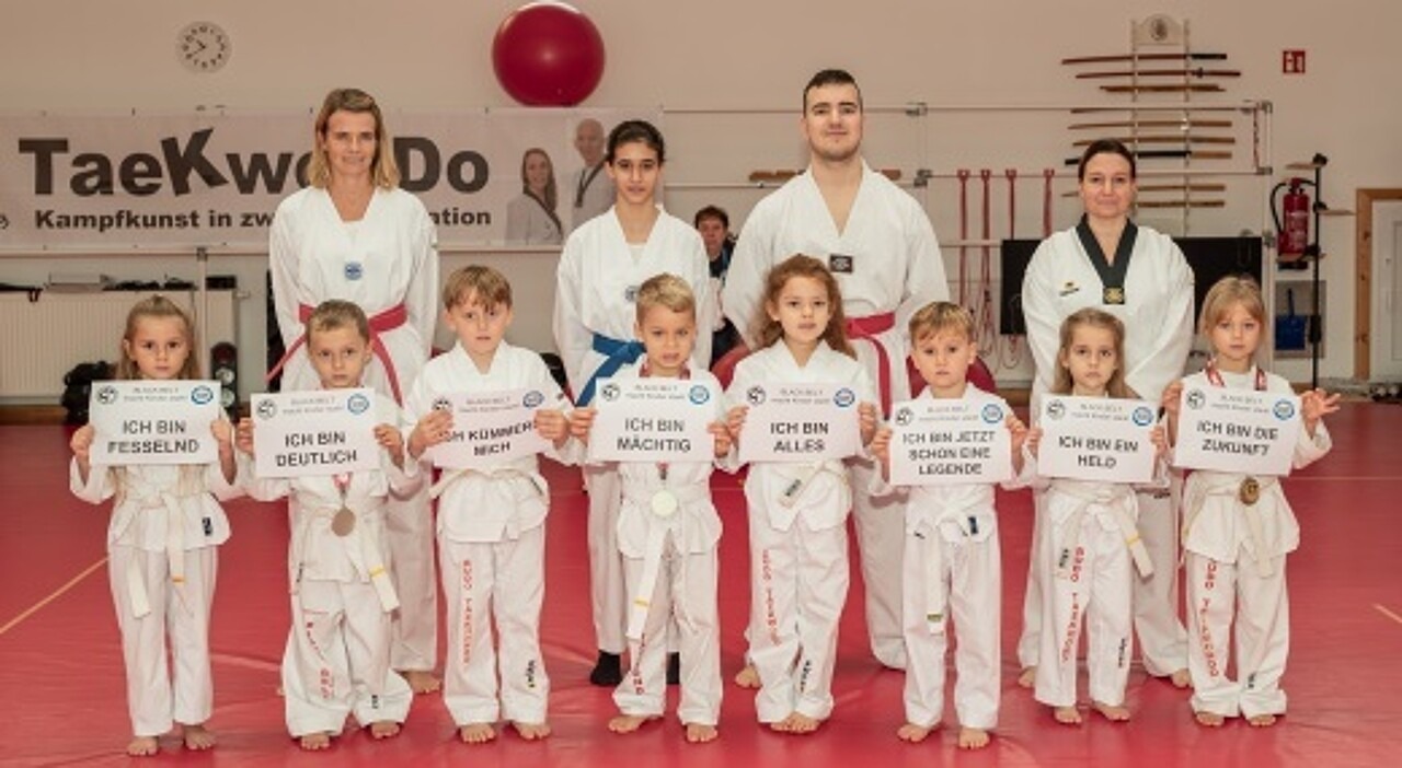 Kinder in Trainingskleidung halten Schilder mit Botschaften wie "Ich bin ein Held." hoch.