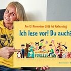 Singa hält ein Werbeplakat zu Vorlesetag mit der Aufschrift „Ich lese vor! Du auch?" hoch.