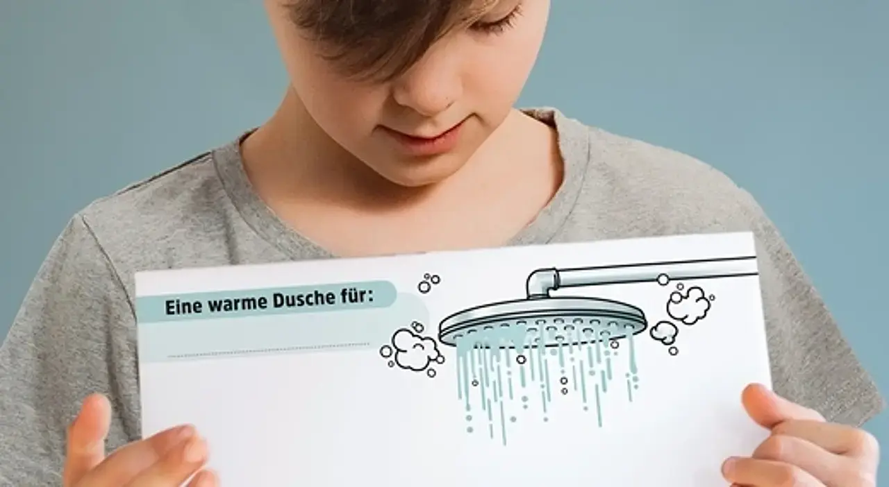 Ein Junge zeigt die PDF-Vorlage für die Warme Dusche mit einem Bild von einem Duschkopf, darunter viel Platz für positive Botschaften.