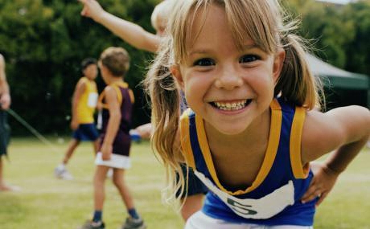 Mädchen im Kindergartenalter in Leichtathletik-Kleidung lächelt in die Kamera