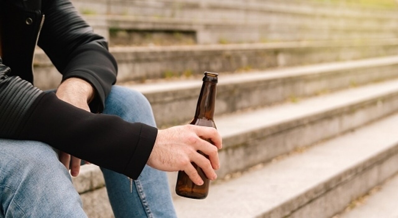 Eine Person sitzt auf einer Treppe und hält eine Flasche Bier fest