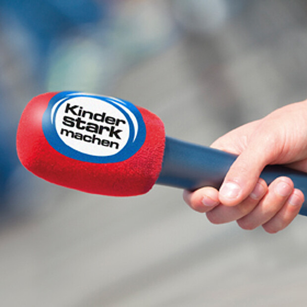 Hand hält rotes Mikrofon mit Kinder stark machen Logo für ein Interview fest